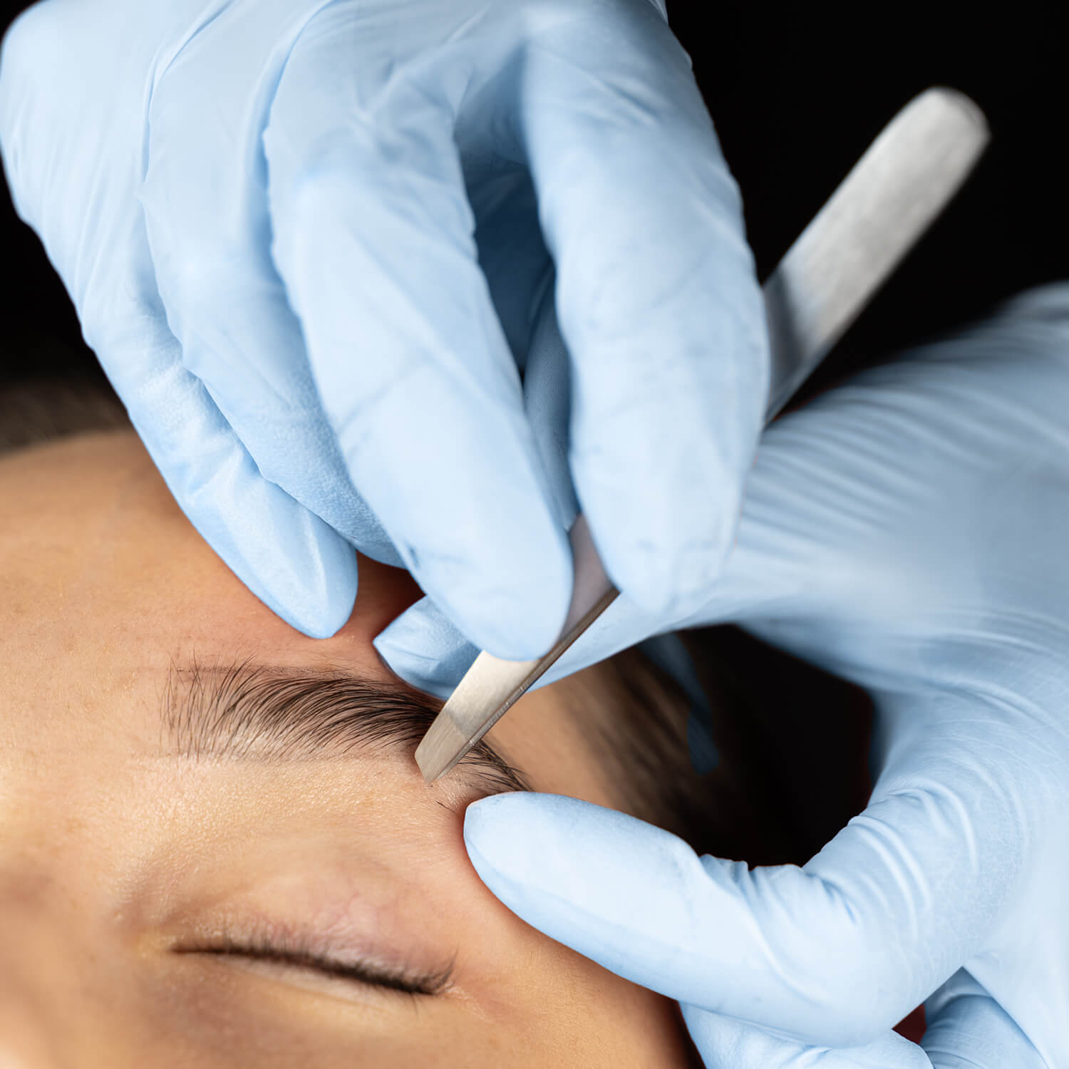 beauticians use professional tweezers to remove a model's eyebrows